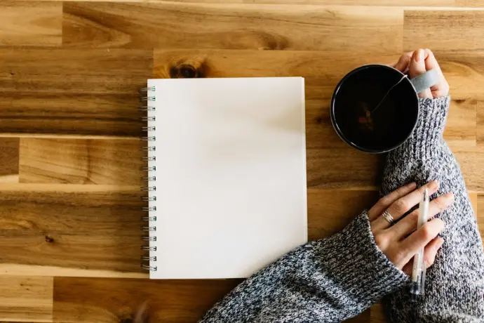 a woman holding a cup of coffee next to a notepad